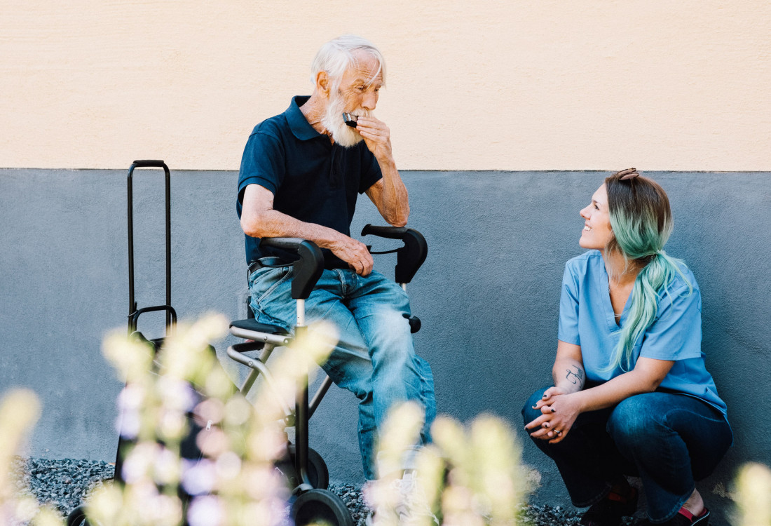 Ein alter Mann spielt Mundharmonika, während eine Pflegerin aufmerksam zuhört.